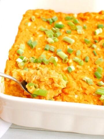 A casserole dish filled with vegetarian buffalo dip with a spoon in it.