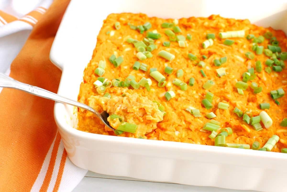 A casserole dish filled with vegetarian buffalo dip with a spoon in it.