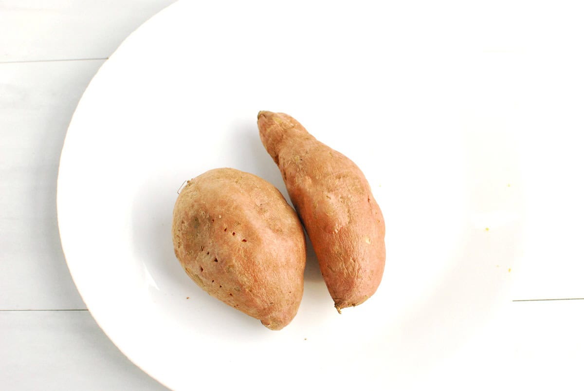 Two sweetpotatoes on a plate after being cooked in the microwave.