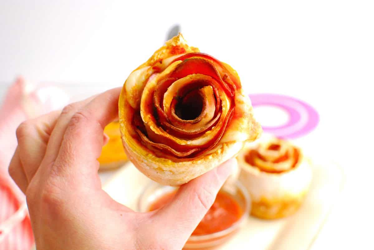 A woman's hand holding a pizza rose.