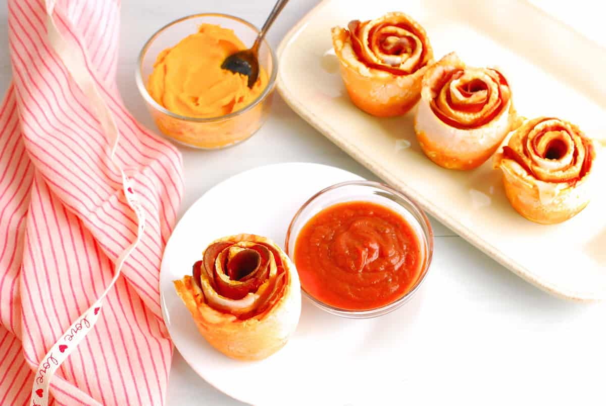 A pizza rose on a plate next to pizza sauce for dipping.