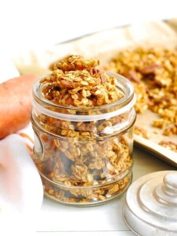 A jar of sweetpotato granola next to a baking sheet and fresh sweetpotato.