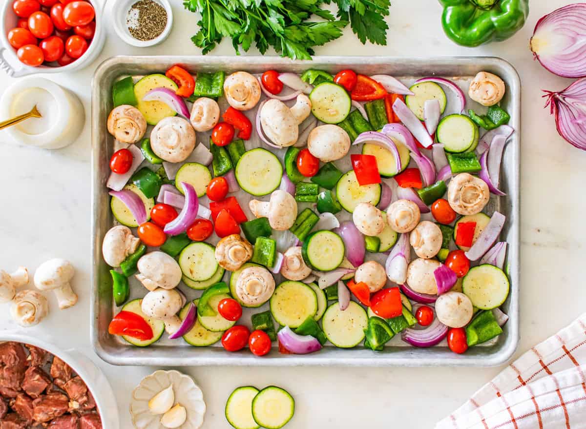 Raw veggies added to a large sheet pan.