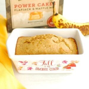 A mini loaf pan with just-baked banana bread, with a banana and box of Kodiak Cakes in the background.