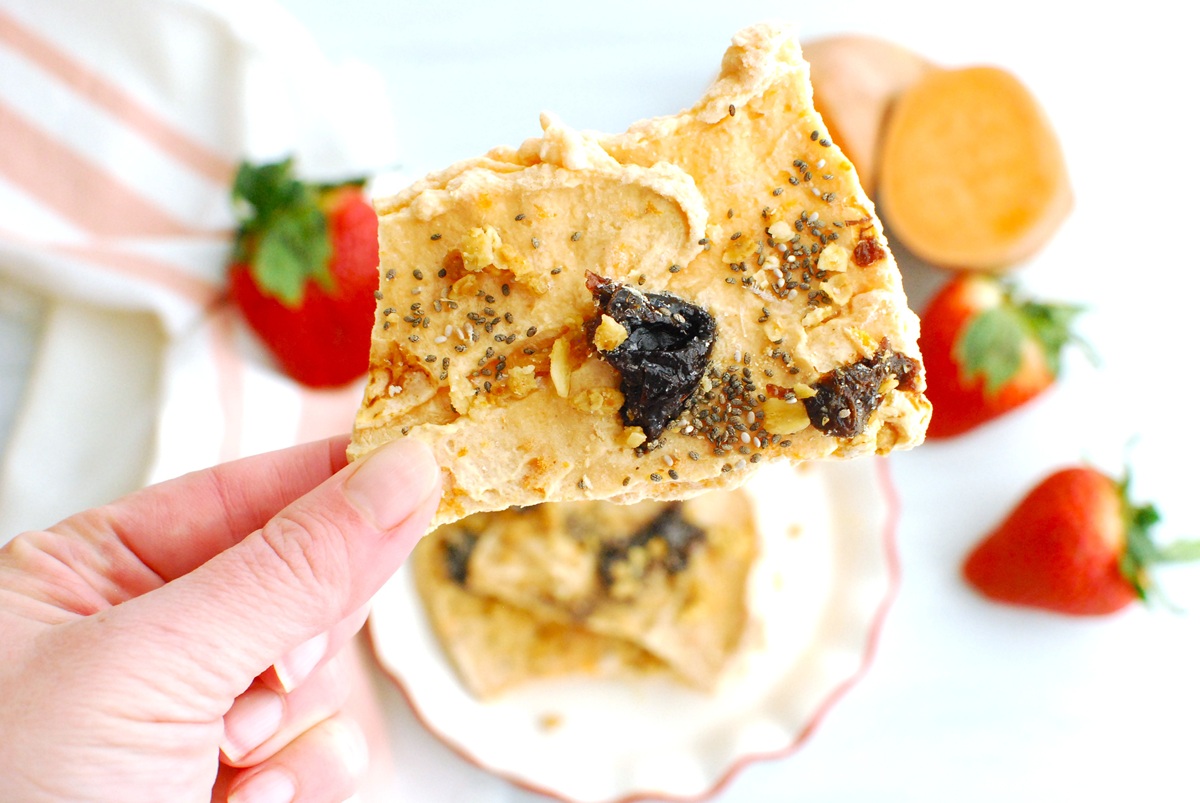 A woman's hand holding sweetpotato yogurt bark topped with prunes, chia seeds, and granola.