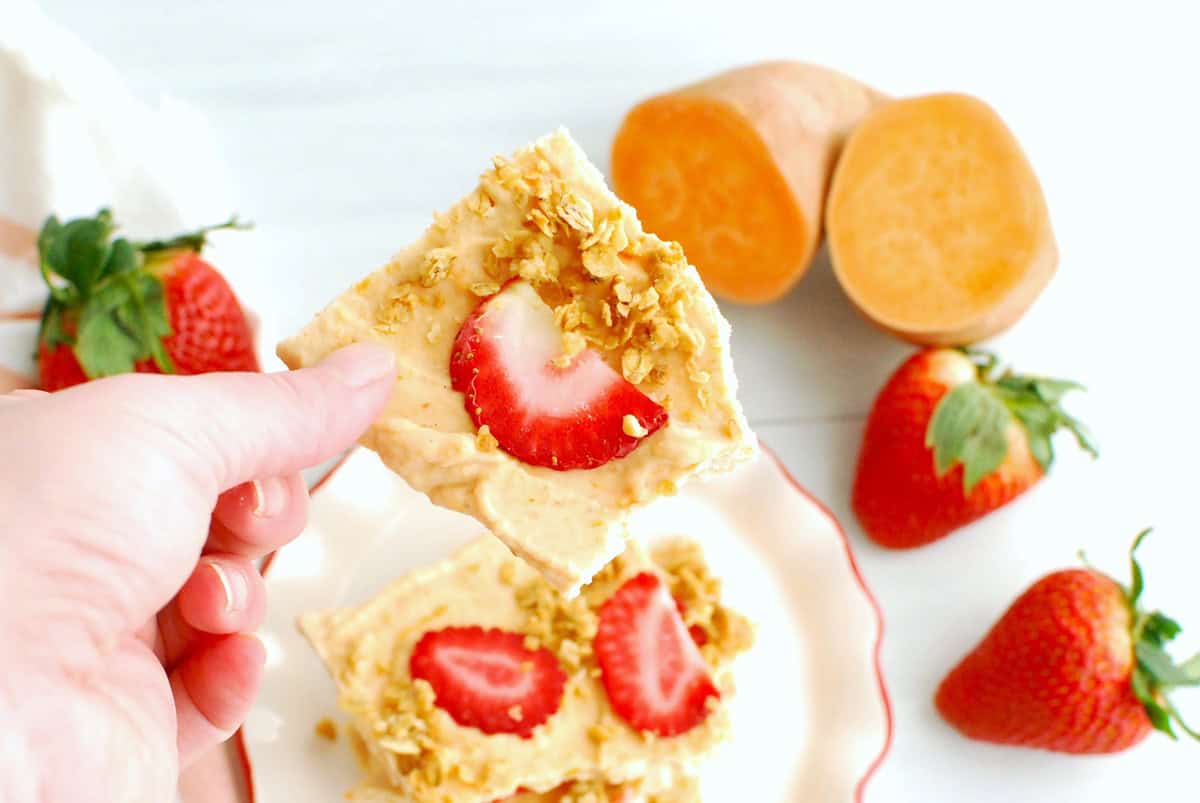 A woman's hand holding sweetpotato yogurt bark topped with strawberries and granola.