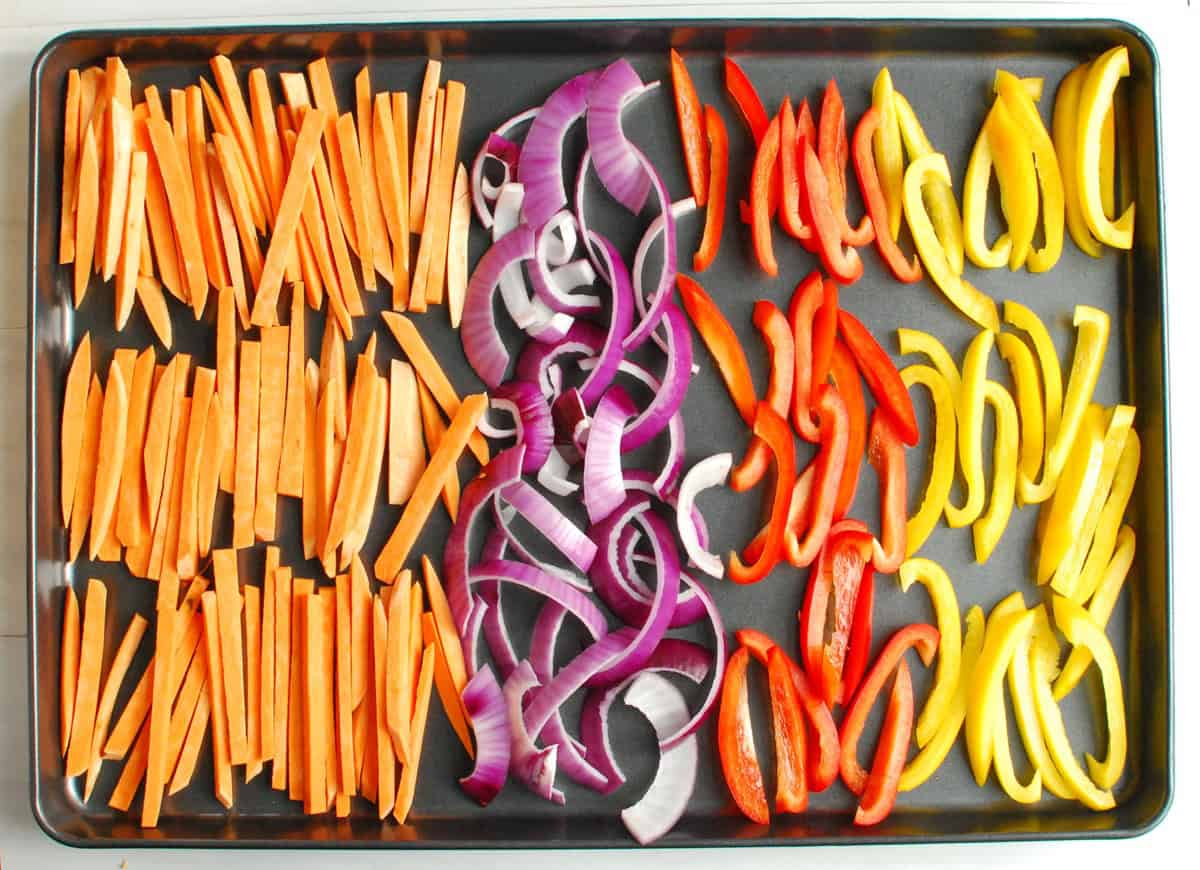 Vegetables chopped up and placed in sections on a sheet pan.