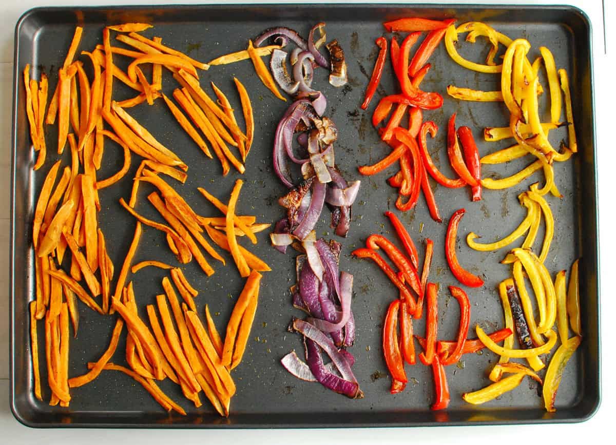 Roasted sweet potatoes, red onions, and bell peppers on a sheet pan.