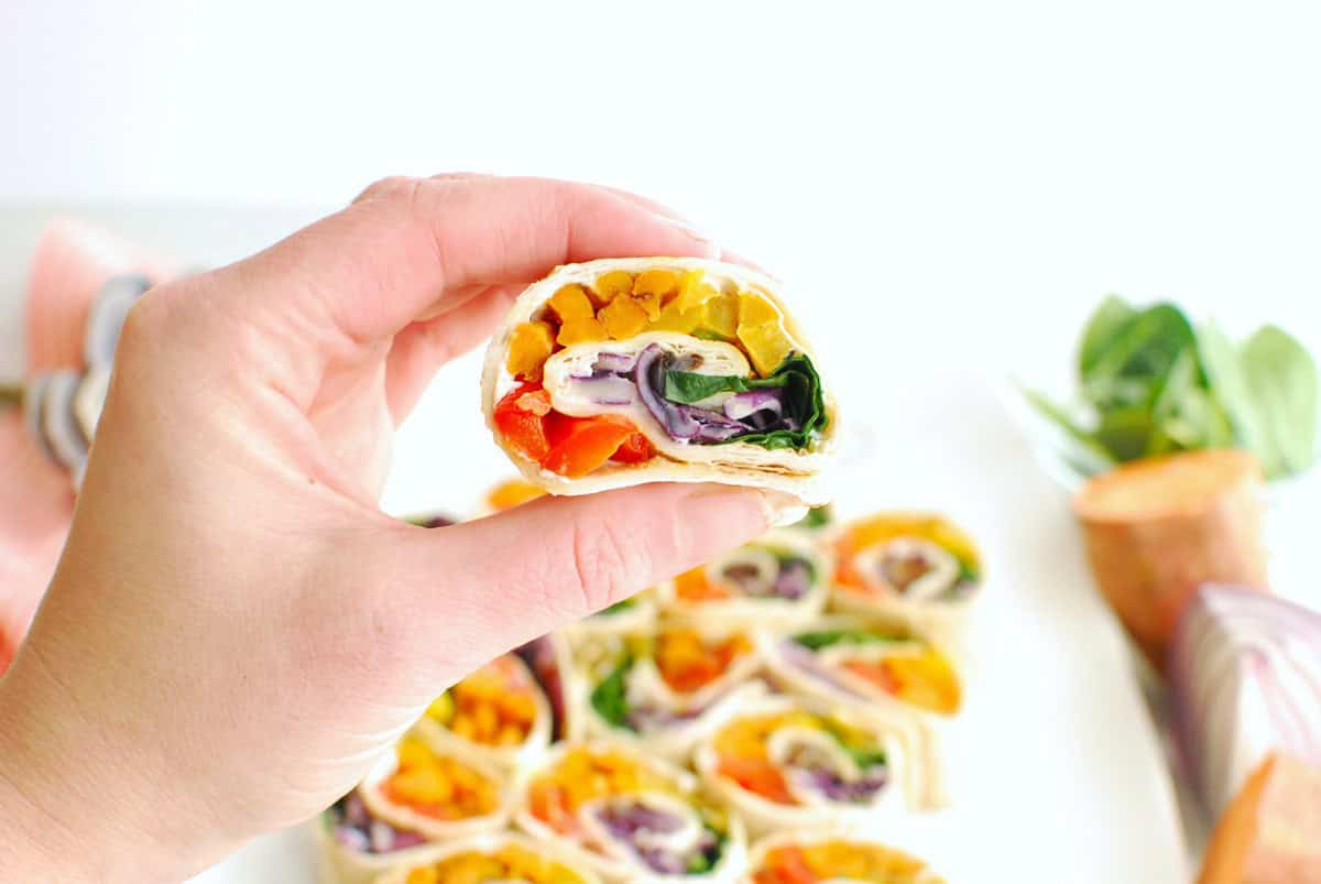 A woman's hand holding a rainbow roasted veggie pinwheel.