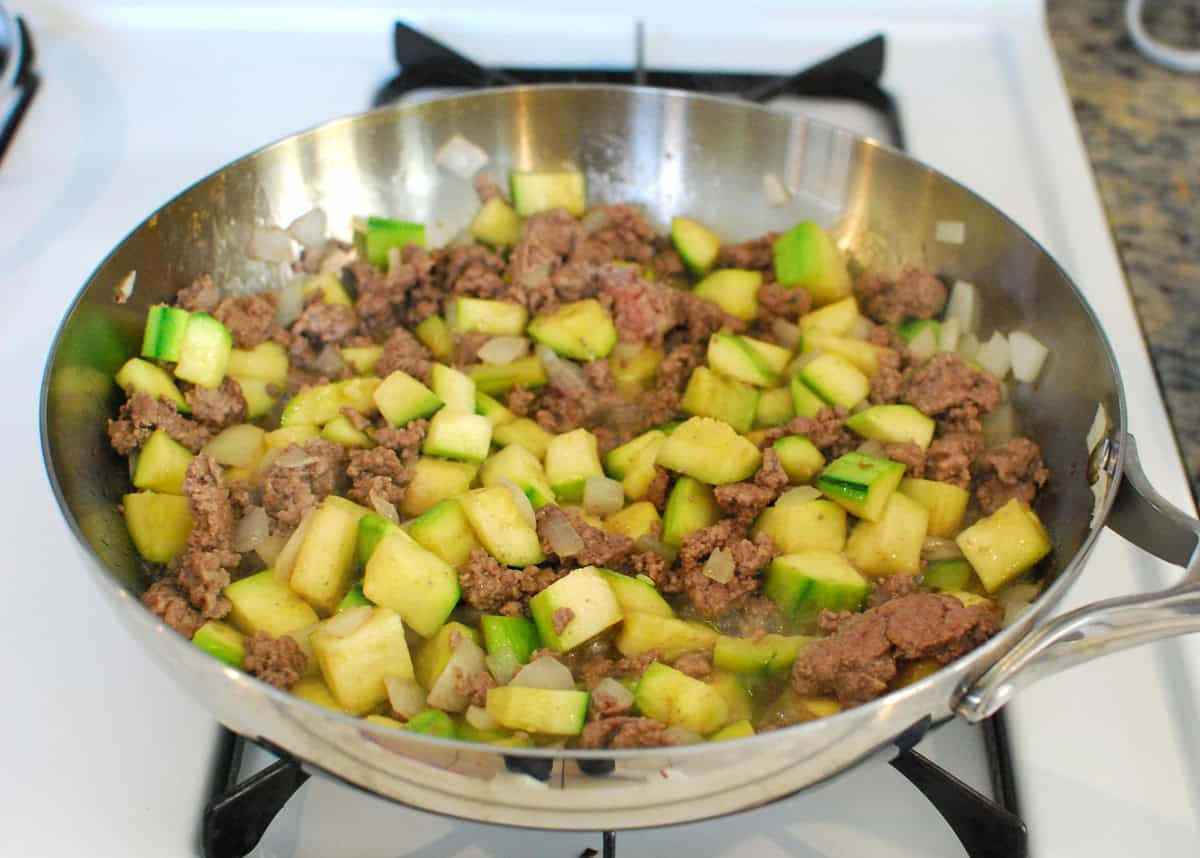 Ground lamb, zucchini, and onion sautéing in a skillet.