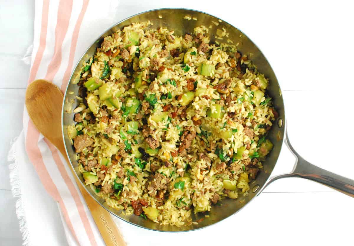 A large skillet filled with spiced lamb, rice, and zucchini.
