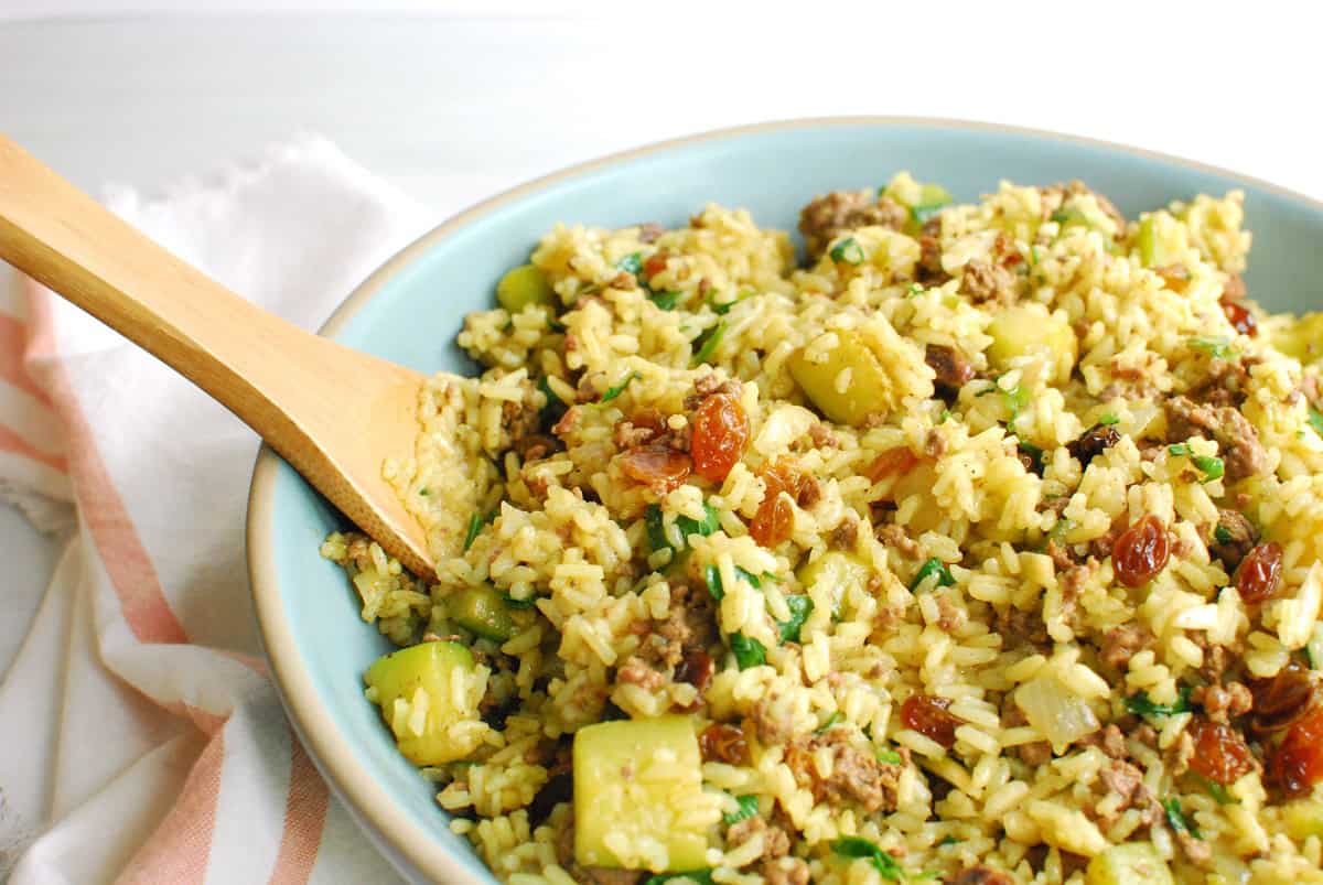 A lamb and rice dish in a bowl with a wooden serving spoon.