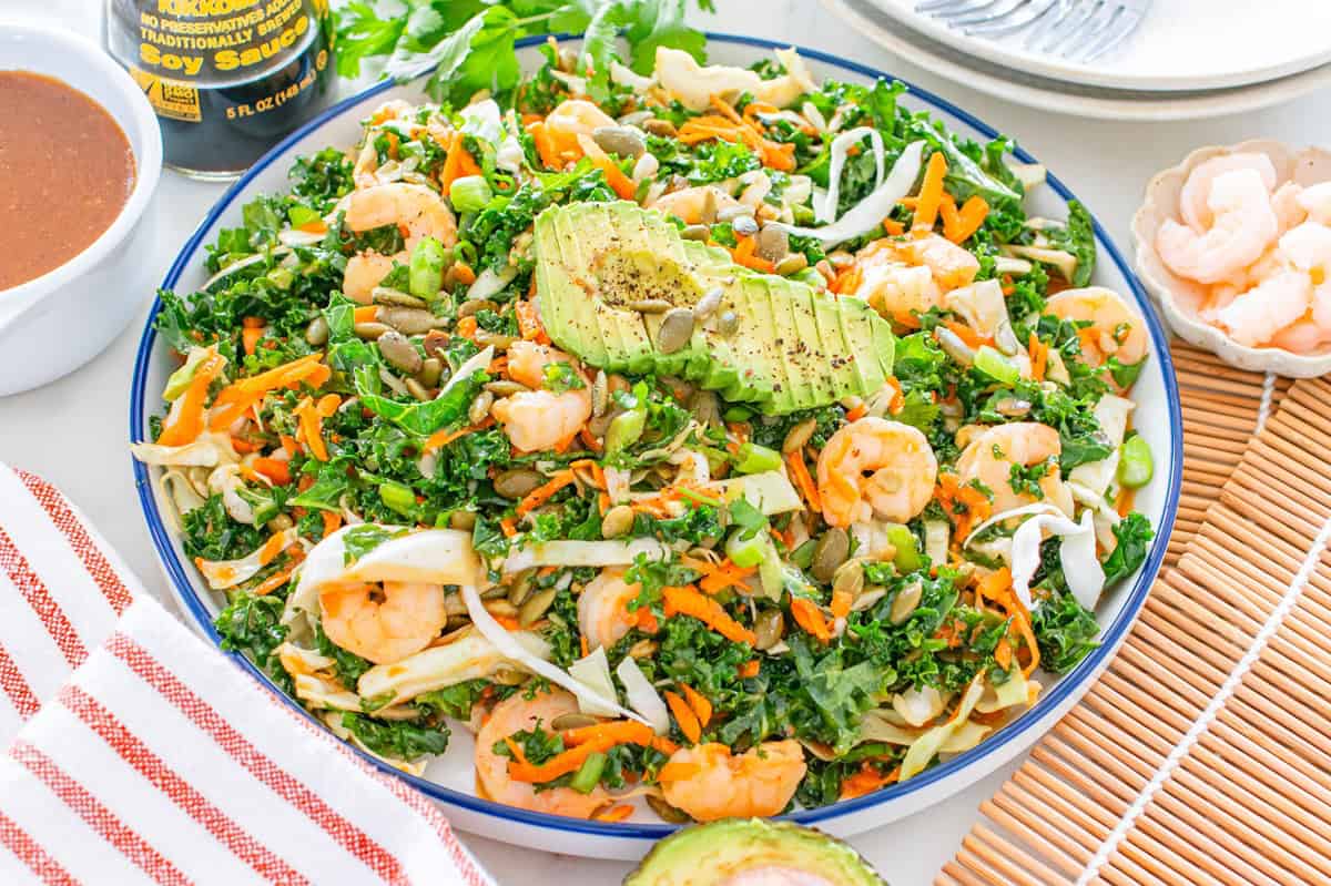 A bowl of kale salad with shrimp, avocado, pepitas, and other ingredients.