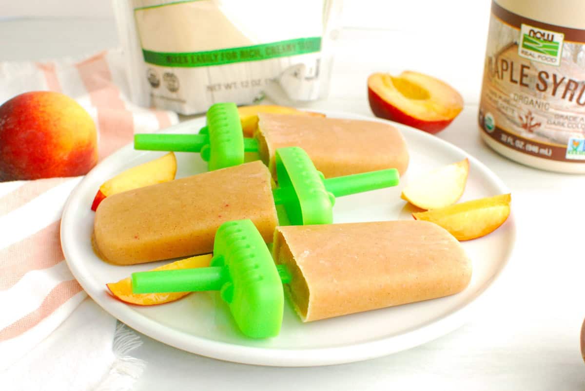 A close up of a peach crisp ice pop with fresh sliced peaches next to it.