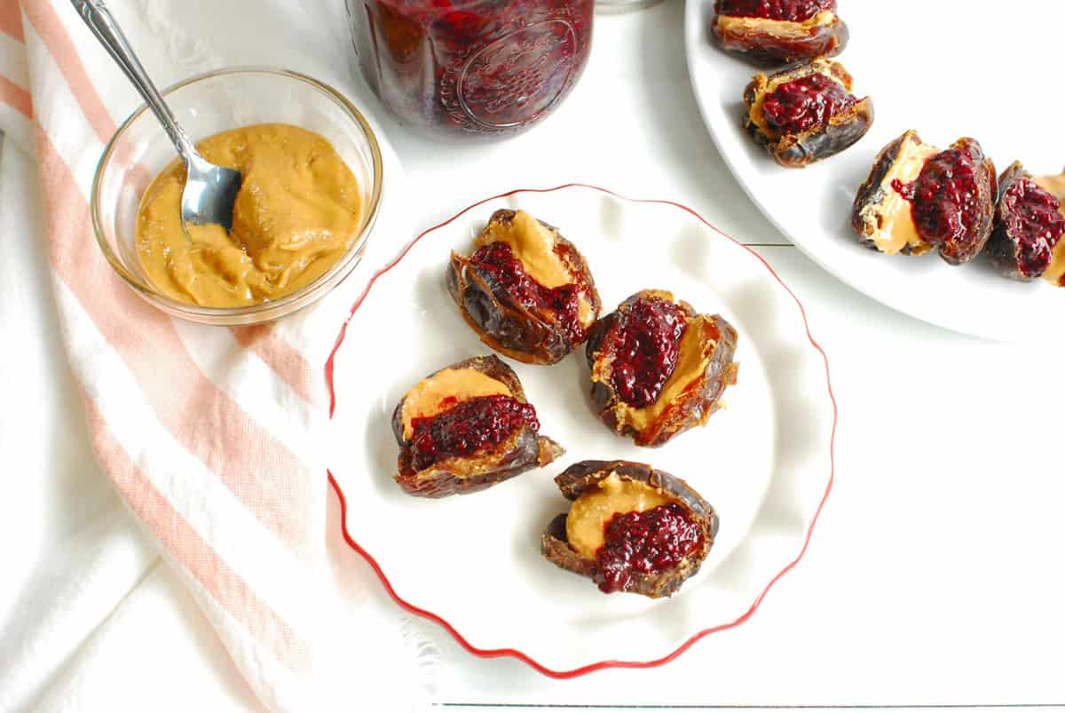 Four PB&J stuffed dates on a plate next to some jam and peanut butter.