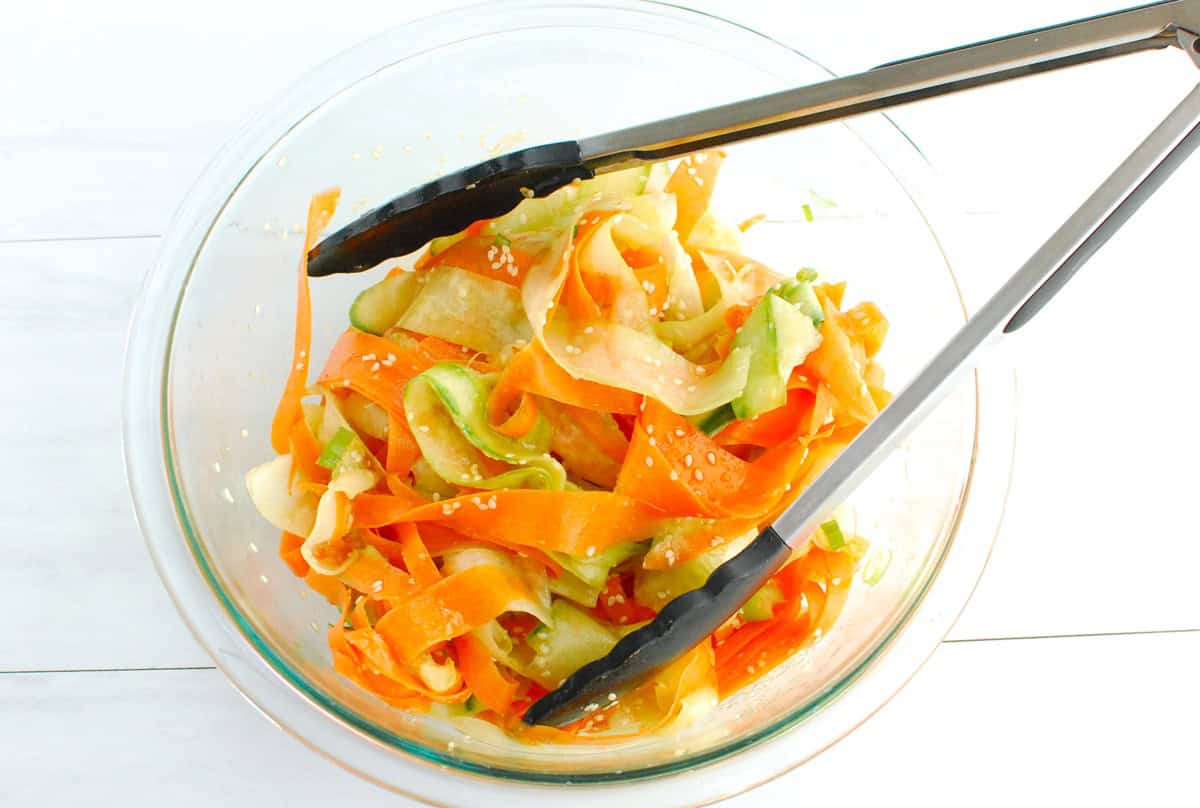 All of the salad ingredients tossed together in a glass mixing bowl with tongs.
