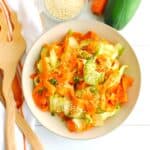 An overhead view of a bowl of sesame cucumber carrot salad next to tongs and a napkin.