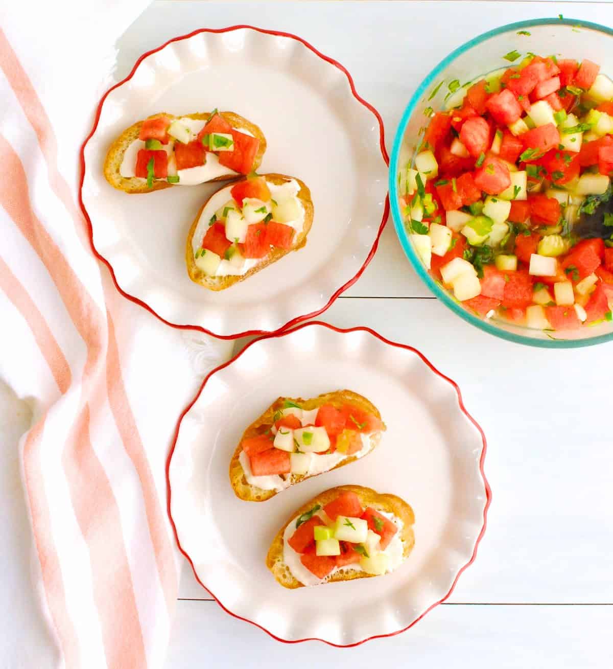 An overhead shot of crostini with whipped feta and watermelon cucumber salsa, next to a bowl of the salsa.
