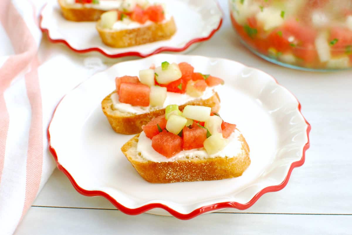 Two crostini with hot honey whipped feta and watermelon cucumber salsa on a plate.