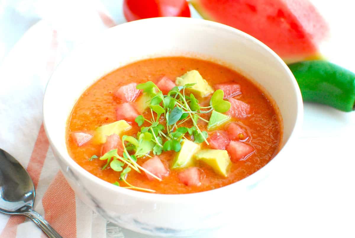 A bowl of watermelon gazpacho garnished with avocado, diced watermelon, and greens.