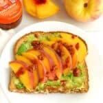 A slice of peach avocado toast topped with chili crisp on a white plate.