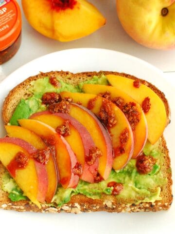 A slice of peach avocado toast topped with chili crisp on a white plate.