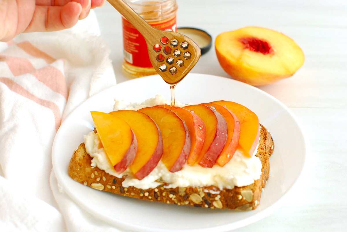 Hot honey being drizzled on a piece of peach ricotta toast.