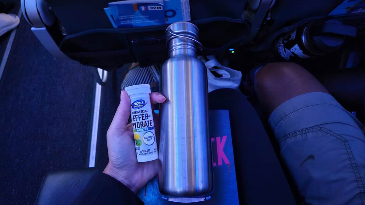 A water bottle and a container of electrolytes in someone's hand on an airplane.