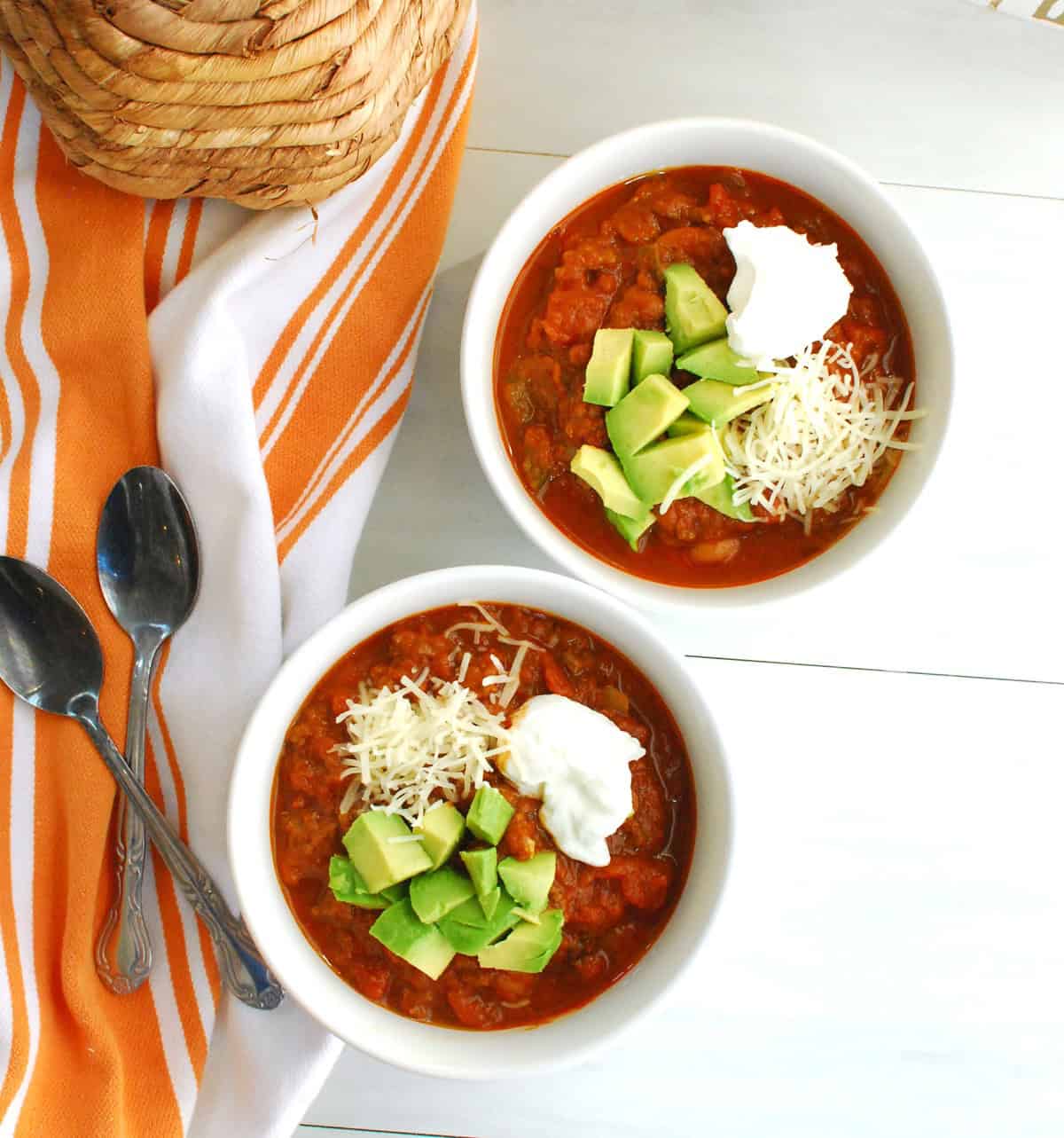 Overhead shot of two bowls of pumpkin chili with spoons next to them.