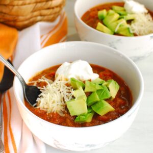 A bowl of pumpkin beer chili topped with avocado, greek yogurt, and cheese.