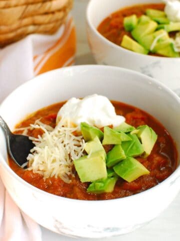 A bowl of pumpkin beer chili topped with avocado, greek yogurt, and cheese.