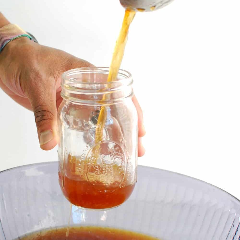 Pouring homemade bone broth into mason jars.