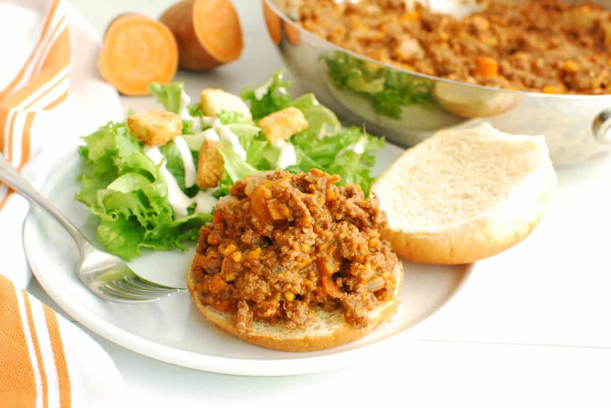 Veggie and beef sloppy joes scooped onto a bun on a plate with salad as well.