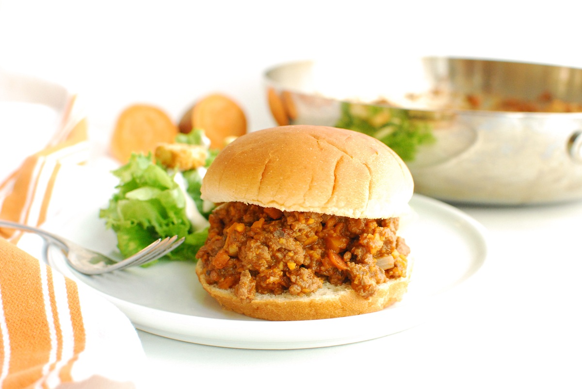 A beef and veggie sloppy joe on a bun on a plate.