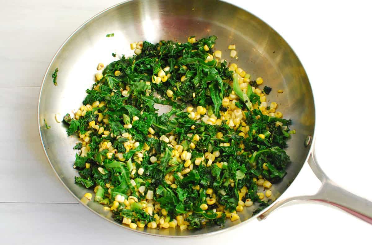 Kale, corn, and green onions sauteed together in a pan.