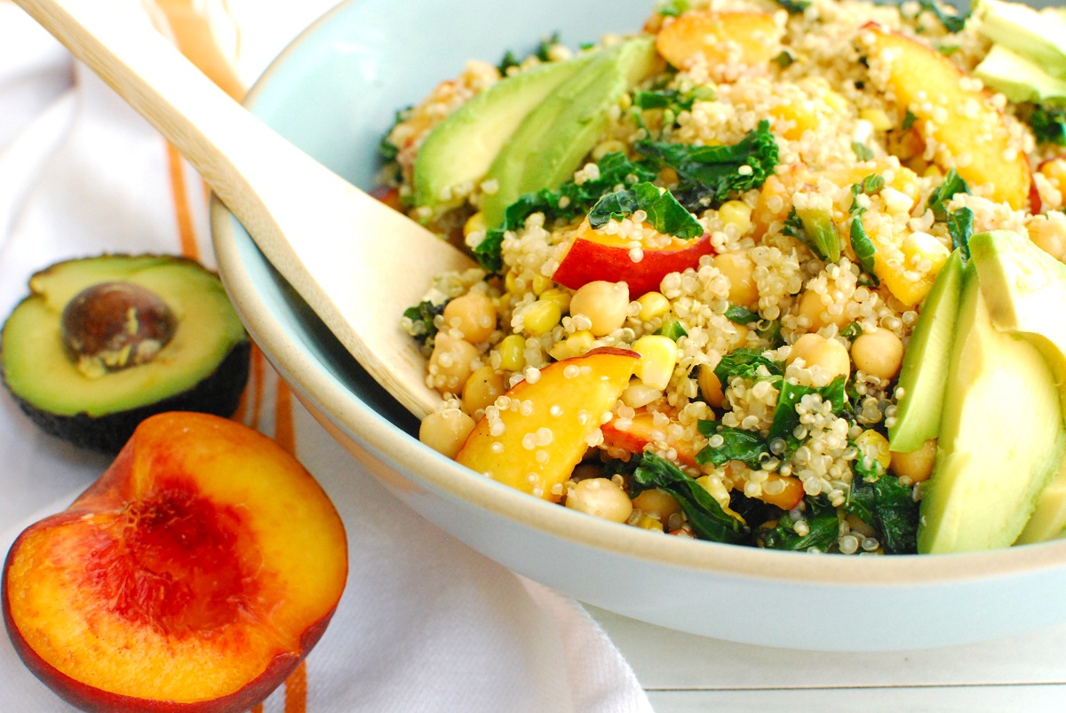 A big bowl of peach quinoa salad with a wooden serving spoon.