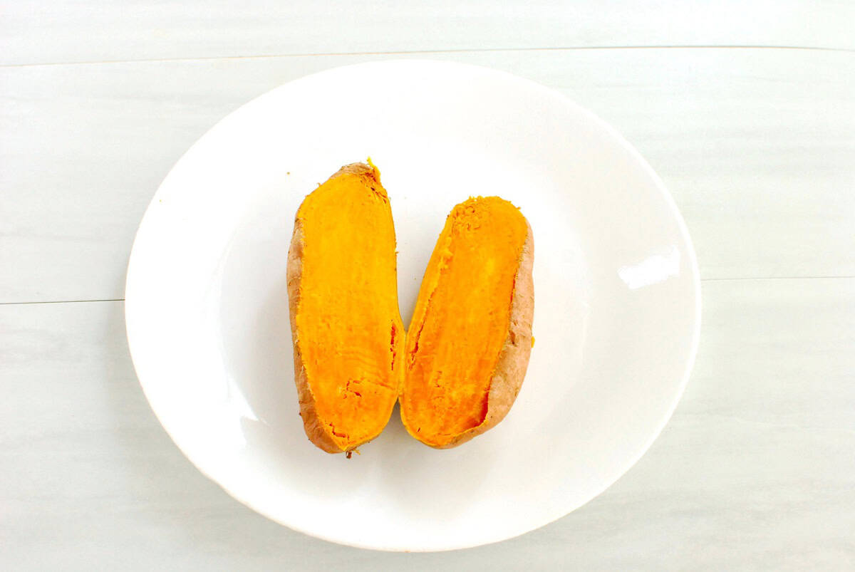 A cooked sweetpotato cut in half on a plate.