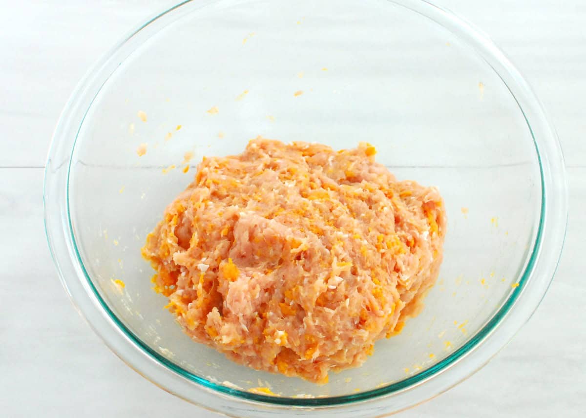 Ground chicken mixed with spices and sweetpotato in a mixing bowl.