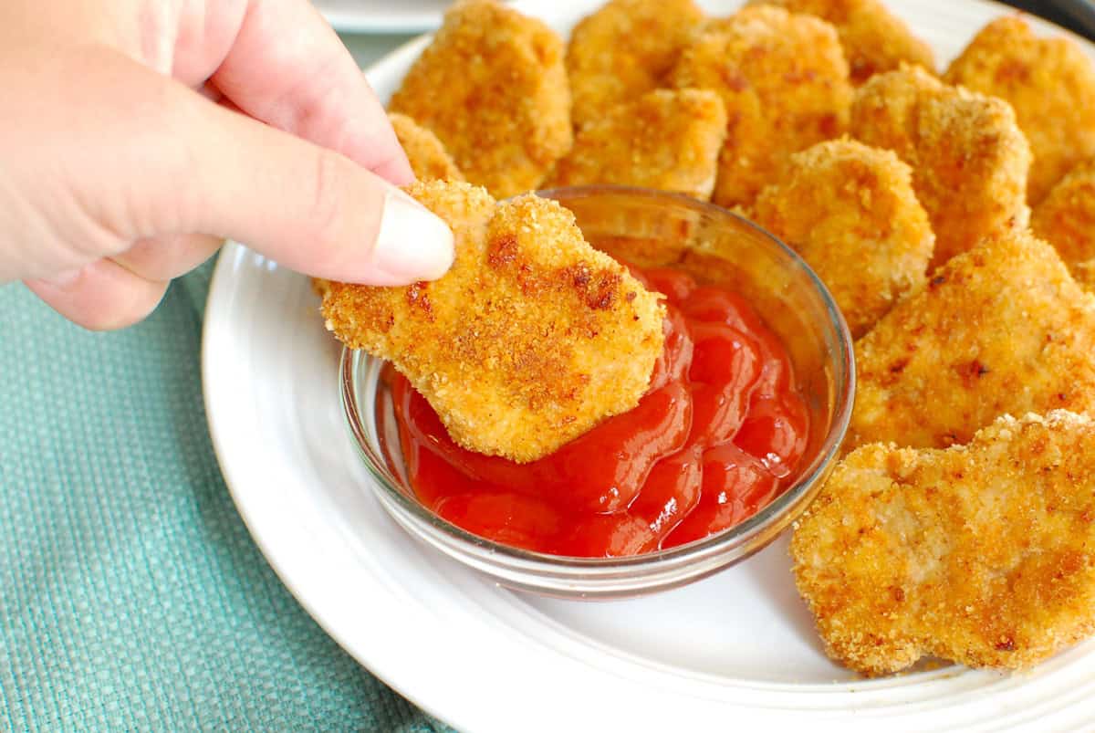 A hand dipping a sweetpotato chicken nugget into ketchup.
