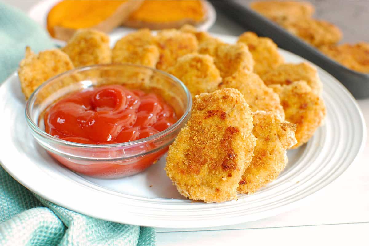 Sweetpotato chicken nuggets on a plate next to a small bowl of ketchup.