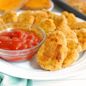 Close up of a sweetpotato chicken nuggets on a white plate next to ketchup.