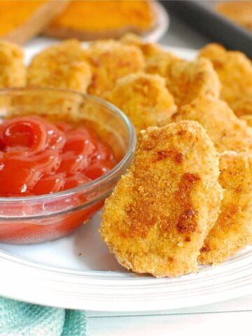 Close up of a sweetpotato chicken nuggets on a white plate next to ketchup.