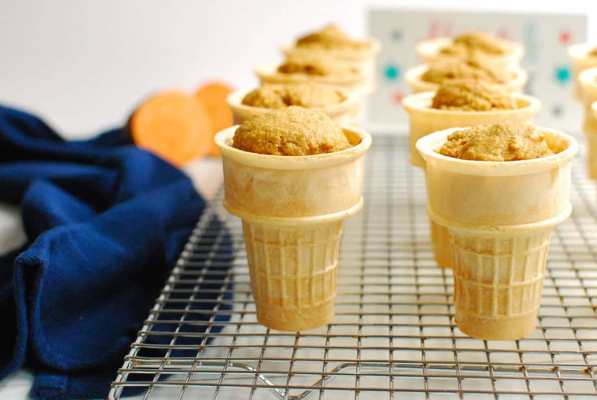 The baked cupcakes in ice cream cones standing on a cooling rack.