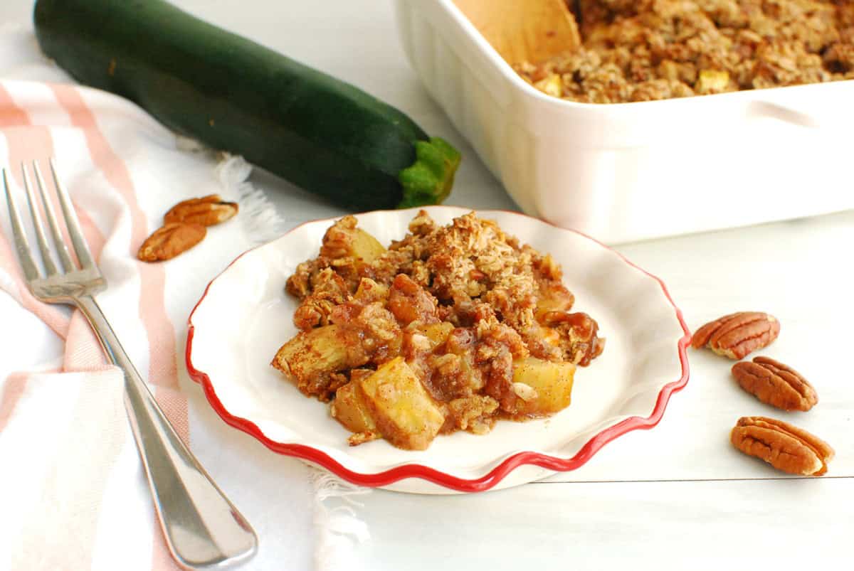 Zucchini crisp on a small plate next to a zucchini and baking dish.