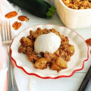 A plate of zucchini crisp topped with ice cream next to a fork and the baking dish.