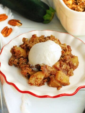 A plate of zucchini crisp topped with ice cream next to a fork and the baking dish.
