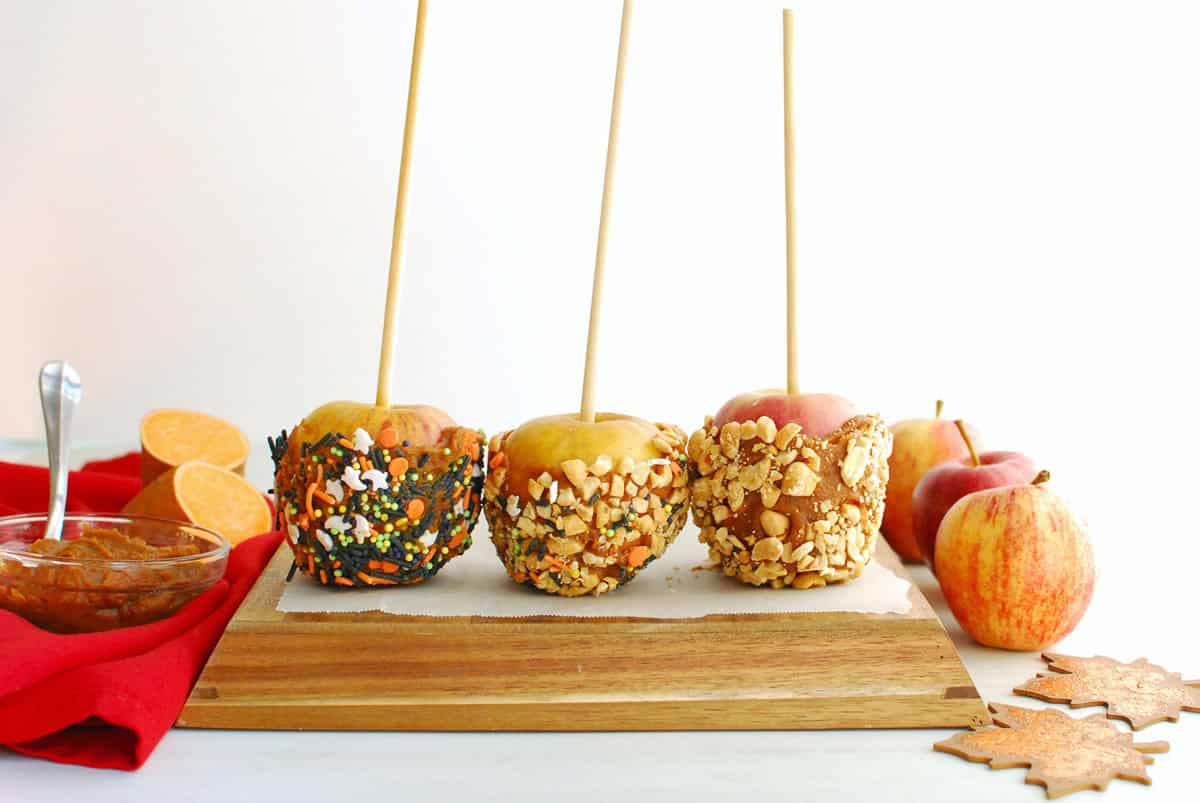 Three caramel apples - one coated in peanuts, one in sprinkles, and one in a combination of both.