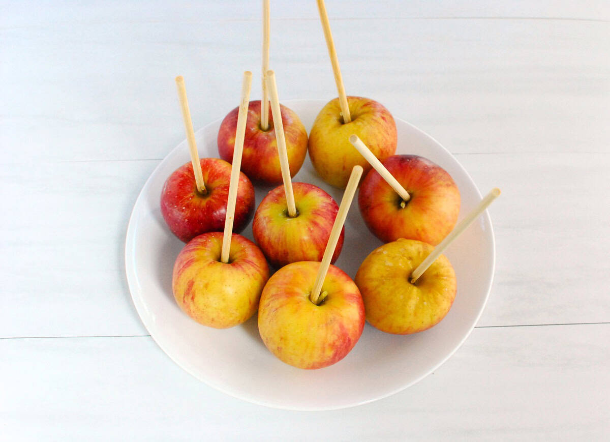 Apples on a plate with wooden sticks pressed into them.