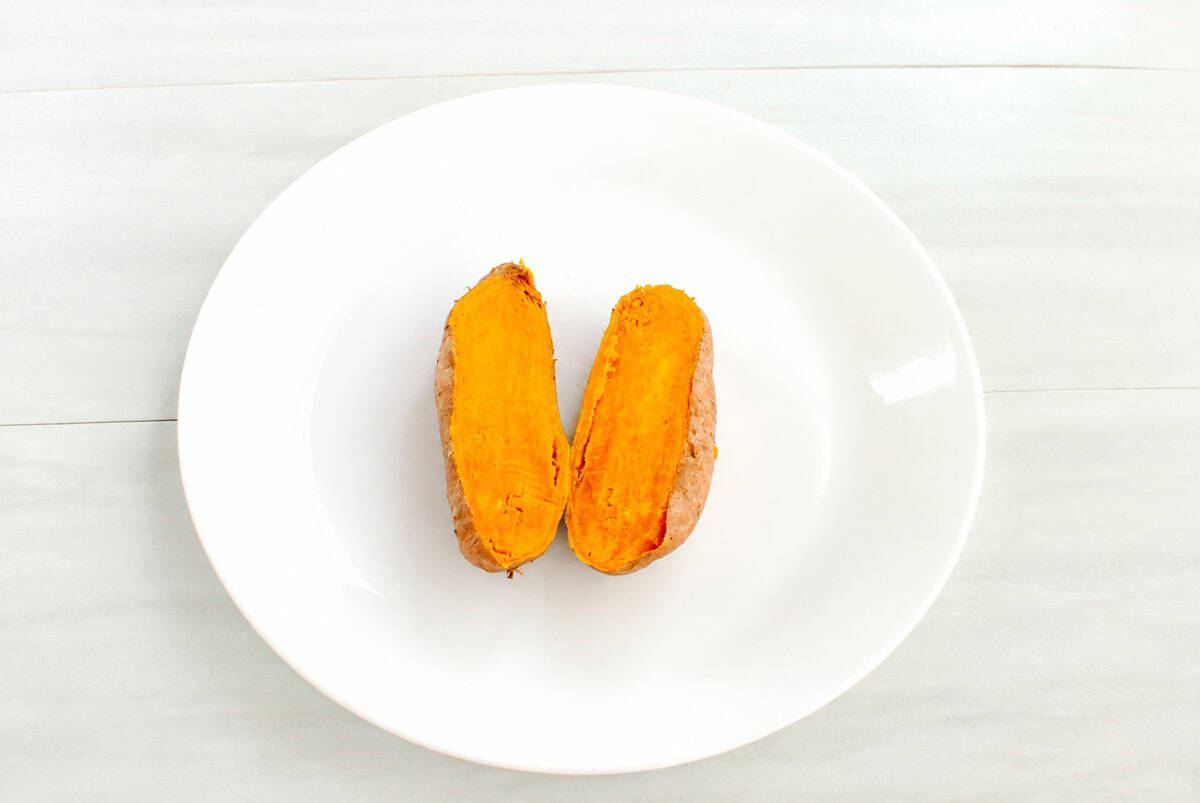 A small sweetpotato on a plate that's cooked and been cut in half.
