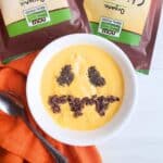 A healthy Halloween smoothie bowl with a jack-o-lantern face made out of chia seeds and cacao nibs.